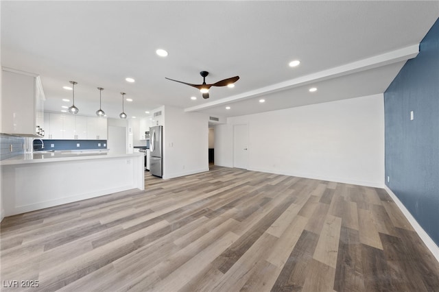 unfurnished living room featuring ceiling fan, sink, beam ceiling, and light wood-type flooring