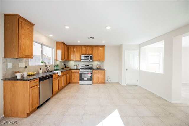 kitchen with stainless steel appliances, backsplash, dark stone counters, and sink