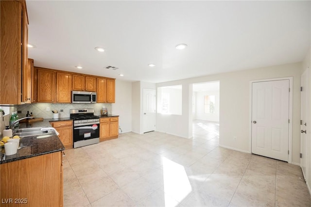 kitchen with backsplash, appliances with stainless steel finishes, sink, and dark stone counters