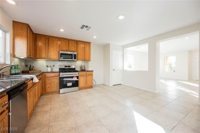 kitchen featuring appliances with stainless steel finishes, tasteful backsplash, light tile patterned flooring, dark stone counters, and sink