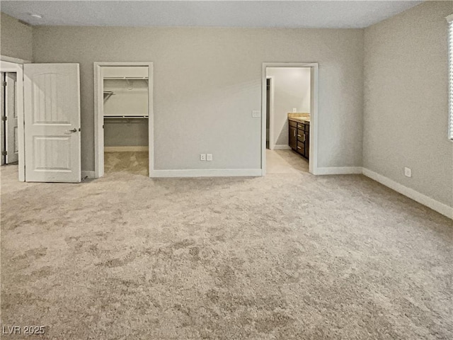 unfurnished bedroom with light carpet, a walk in closet, a closet, and connected bathroom