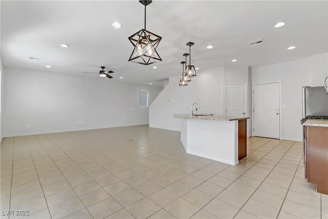 kitchen featuring light tile patterned floors, ceiling fan, hanging light fixtures, stainless steel refrigerator, and light stone countertops