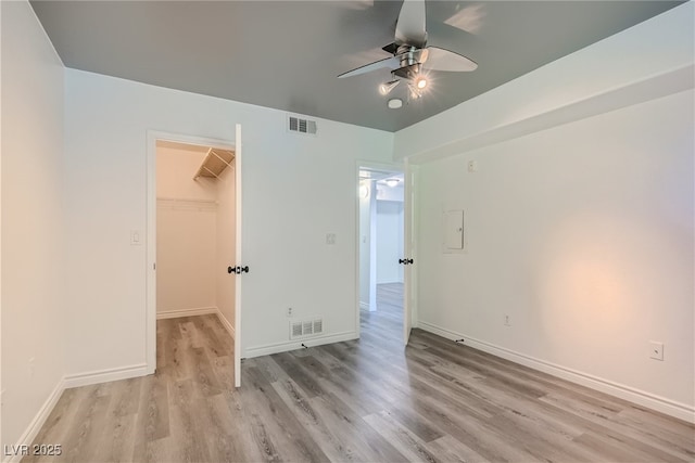 unfurnished bedroom featuring ceiling fan, a walk in closet, a closet, and light hardwood / wood-style flooring