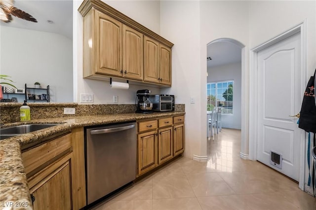 kitchen featuring light tile patterned floors, ceiling fan, dark stone counters, stainless steel dishwasher, and sink