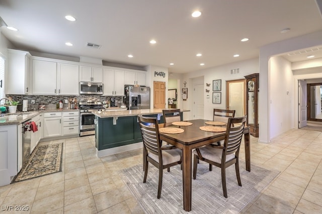 kitchen with stainless steel appliances, light stone countertops, a kitchen island, and white cabinets