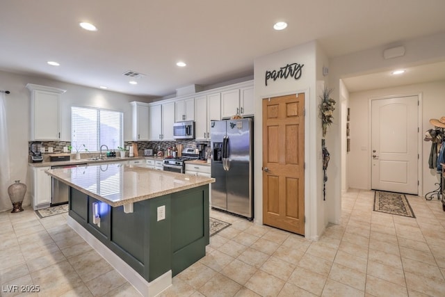 kitchen featuring white cabinetry, sink, a center island, stainless steel appliances, and light stone countertops