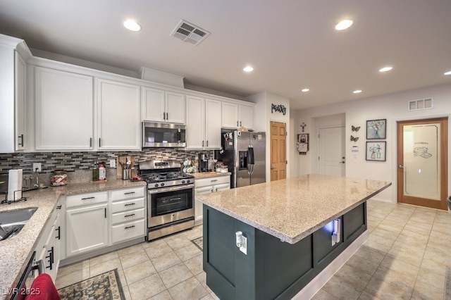 kitchen with light stone counters, appliances with stainless steel finishes, a center island, and white cabinets