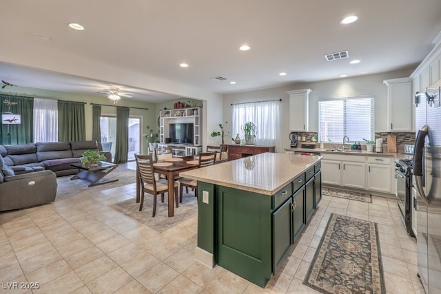 kitchen with sink, black gas range, backsplash, a center island, and white cabinets