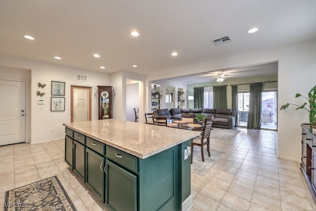 kitchen featuring ceiling fan, green cabinets, a kitchen island, light stone counters, and light tile patterned flooring