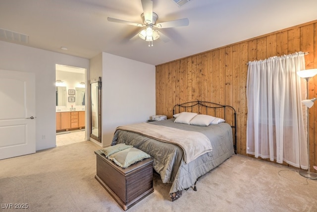 bedroom with ceiling fan, light carpet, ensuite bath, and wood walls