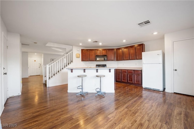 kitchen featuring a kitchen island, a kitchen bar, dark wood-type flooring, white fridge, and stove