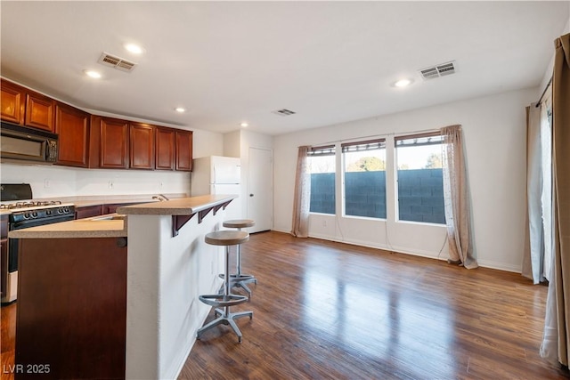 kitchen featuring a kitchen bar, sink, dark wood-type flooring, range with gas stovetop, and a center island