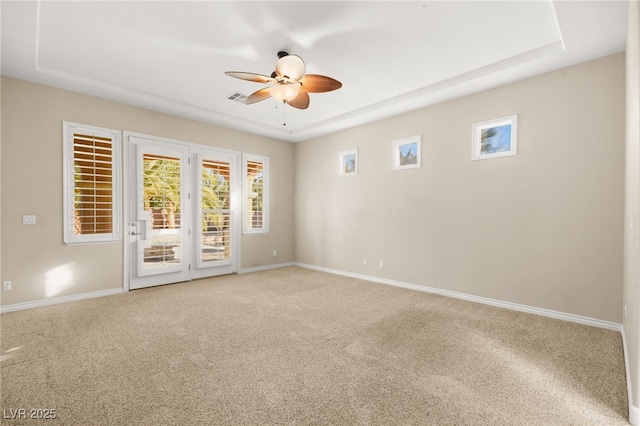 empty room with carpet floors, a raised ceiling, and ceiling fan