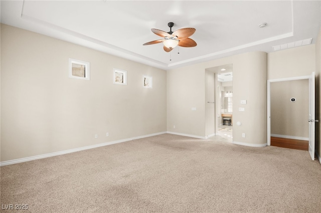 unfurnished room with ceiling fan, a tray ceiling, and light carpet