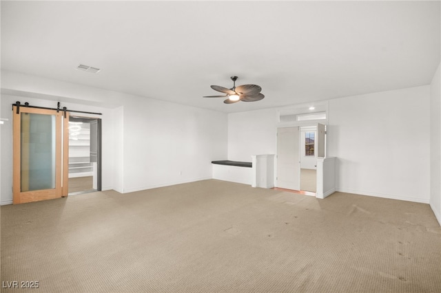 unfurnished living room featuring ceiling fan, a barn door, and carpet flooring