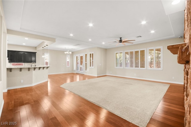 unfurnished living room with a raised ceiling, ceiling fan with notable chandelier, hardwood / wood-style floors, and sink