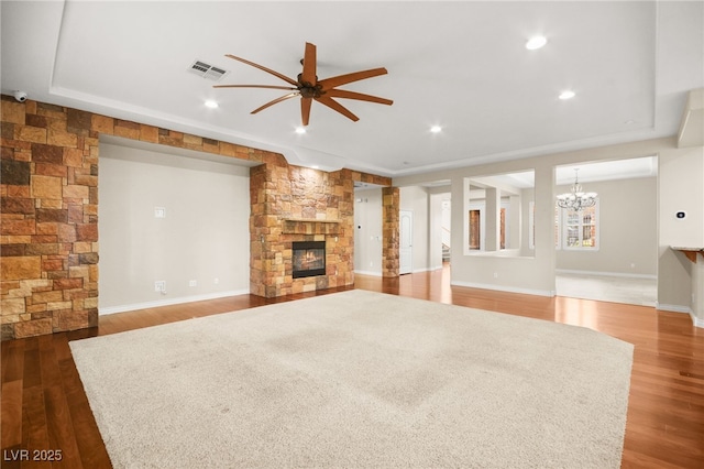 unfurnished living room featuring ceiling fan with notable chandelier, dark hardwood / wood-style flooring, and a stone fireplace