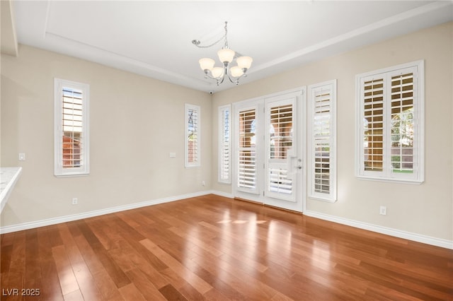 unfurnished room featuring hardwood / wood-style flooring, plenty of natural light, and a notable chandelier