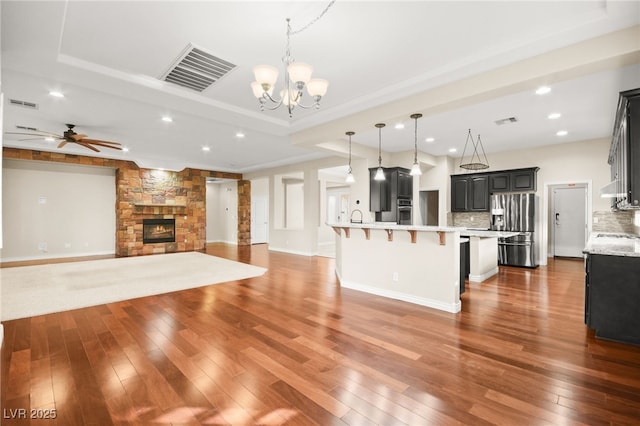 kitchen featuring decorative light fixtures, decorative backsplash, a kitchen breakfast bar, a stone fireplace, and stainless steel appliances