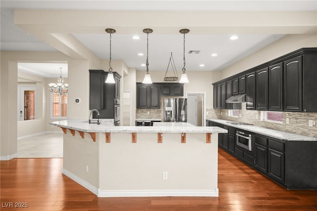 kitchen with hardwood / wood-style floors, appliances with stainless steel finishes, backsplash, a notable chandelier, and pendant lighting