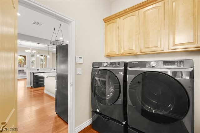 laundry area featuring cabinets, washer and clothes dryer, light hardwood / wood-style flooring, and a chandelier