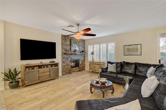 living room featuring ceiling fan, light hardwood / wood-style flooring, and a stone fireplace