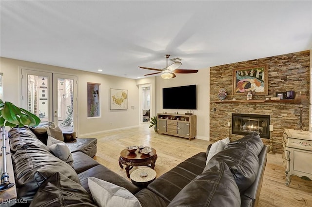 living room featuring ceiling fan, a stone fireplace, and light hardwood / wood-style flooring