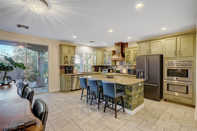 kitchen with a wealth of natural light, appliances with stainless steel finishes, a kitchen island, wall chimney range hood, and a kitchen breakfast bar