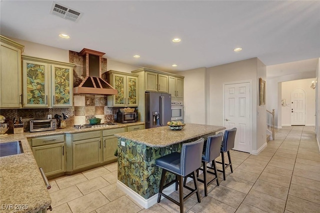 kitchen with light tile patterned floors, stainless steel appliances, backsplash, wall chimney range hood, and a center island