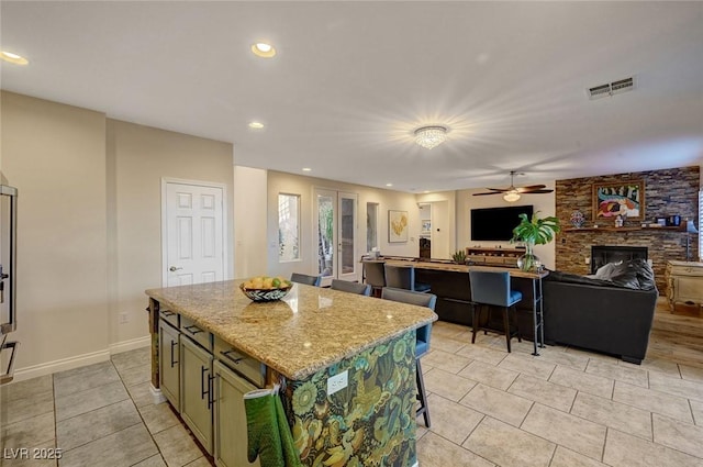 kitchen featuring light stone countertops, a kitchen island, a fireplace, light tile patterned flooring, and ceiling fan