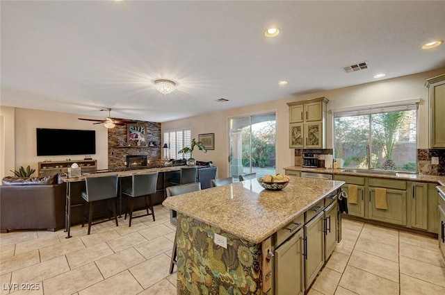 kitchen with a kitchen island, a stone fireplace, tasteful backsplash, ceiling fan, and light tile patterned floors