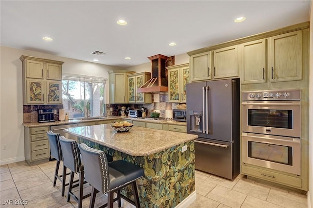 kitchen featuring a center island, decorative backsplash, stainless steel appliances, light tile patterned floors, and wall chimney exhaust hood