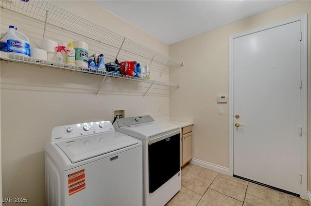 clothes washing area featuring light tile patterned floors, washing machine and dryer, and cabinets