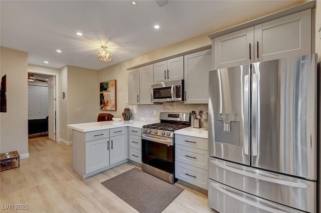 kitchen with kitchen peninsula, stainless steel appliances, gray cabinetry, tasteful backsplash, and light hardwood / wood-style flooring