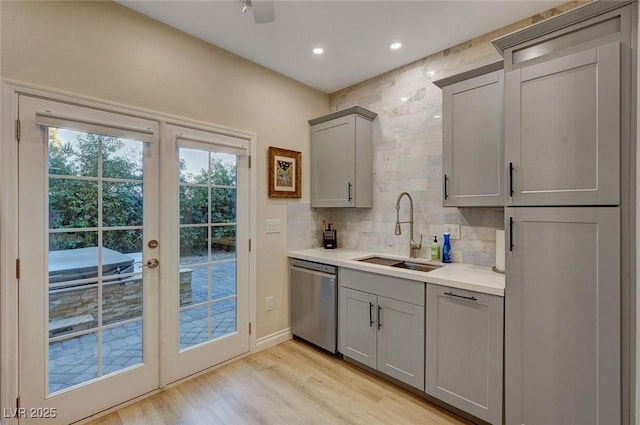 kitchen with gray cabinetry, tasteful backsplash, light wood-type flooring, dishwasher, and sink