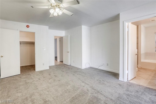 unfurnished bedroom featuring ceiling fan, connected bathroom, a walk in closet, and light carpet