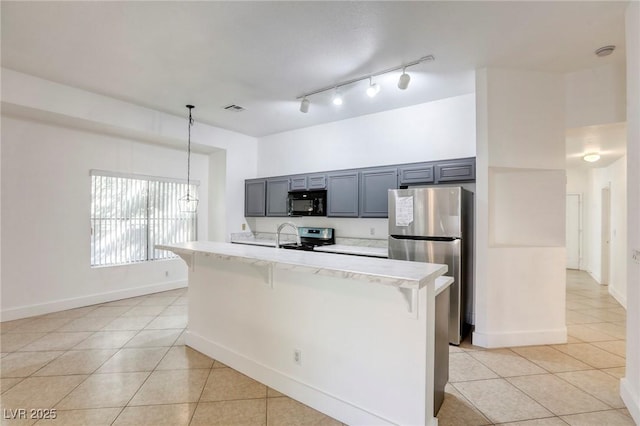 kitchen with pendant lighting, appliances with stainless steel finishes, a kitchen bar, an island with sink, and light tile patterned floors