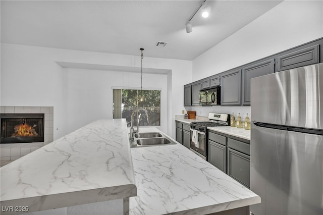 kitchen with a center island with sink, stainless steel appliances, track lighting, hanging light fixtures, and sink