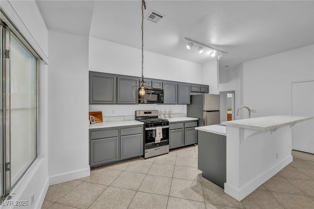 kitchen with a center island with sink, hanging light fixtures, a kitchen breakfast bar, gray cabinetry, and stainless steel appliances