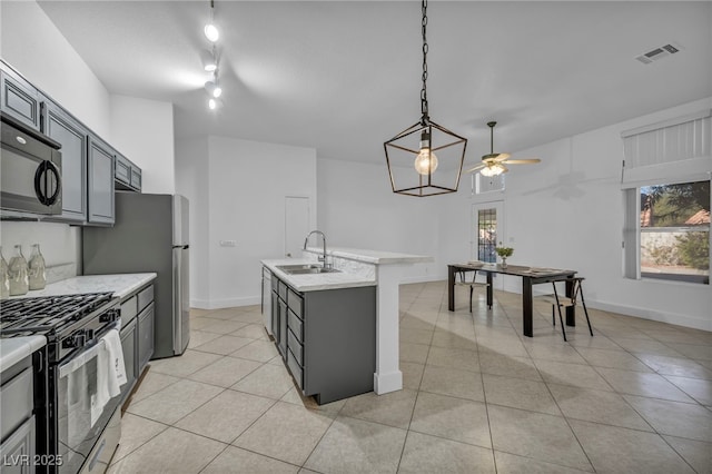 kitchen with stainless steel gas range, gray cabinetry, an island with sink, and sink