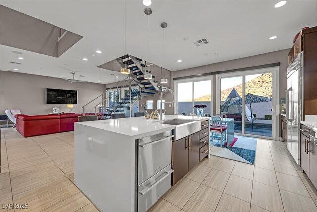 kitchen featuring sink, hanging light fixtures, dark brown cabinetry, and an island with sink