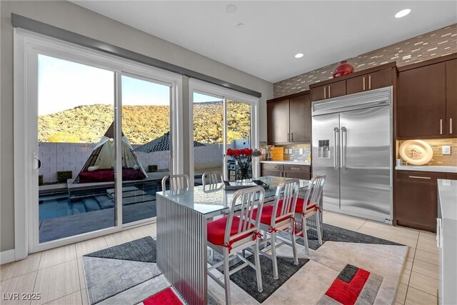 kitchen featuring light tile patterned floors, a breakfast bar area, built in fridge, dark brown cabinetry, and a center island