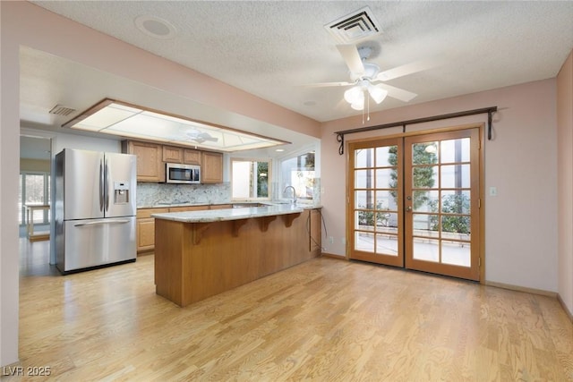 kitchen featuring appliances with stainless steel finishes, backsplash, kitchen peninsula, ceiling fan, and light hardwood / wood-style flooring