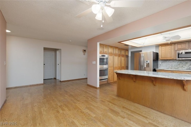 kitchen featuring tasteful backsplash, kitchen peninsula, light wood-type flooring, a breakfast bar area, and stainless steel appliances