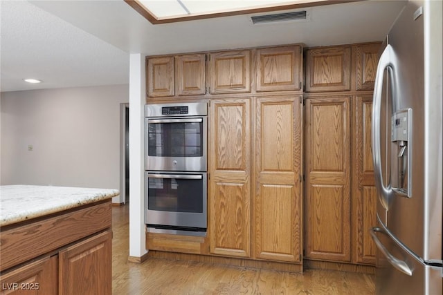 kitchen with stainless steel appliances, light hardwood / wood-style flooring, and light stone counters