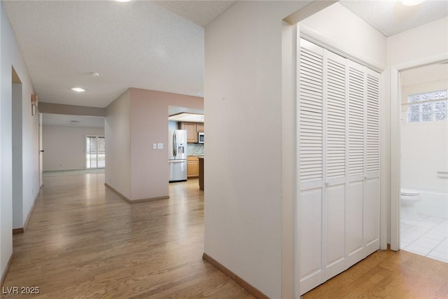 hallway with a textured ceiling and light hardwood / wood-style flooring