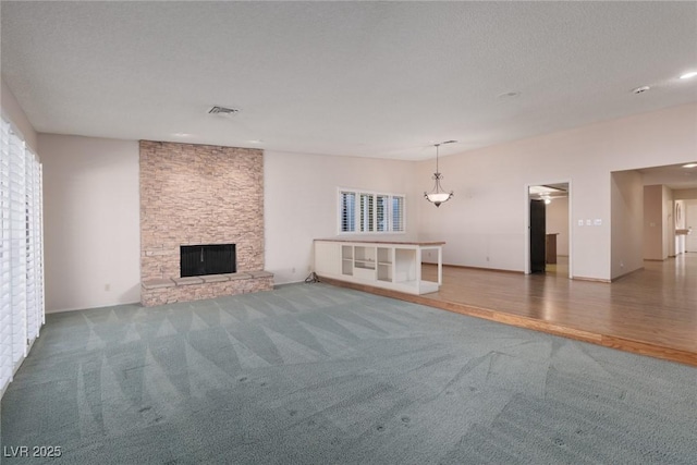 unfurnished living room with ceiling fan, a fireplace, a textured ceiling, and carpet flooring