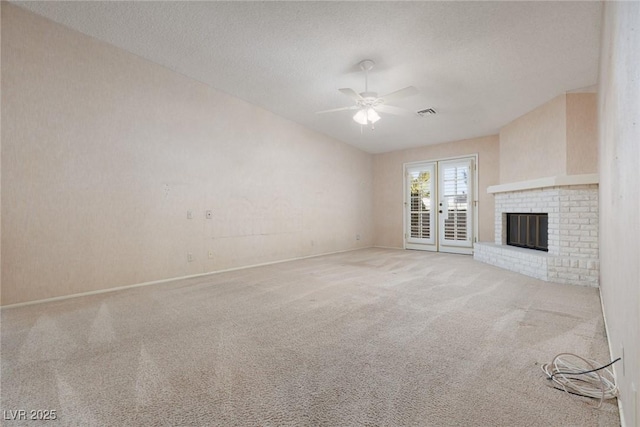 unfurnished living room featuring ceiling fan, light colored carpet, a textured ceiling, and a fireplace