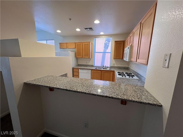 kitchen with light stone counters, sink, white appliances, and kitchen peninsula