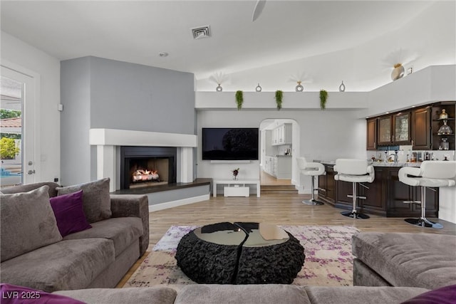 living room featuring light hardwood / wood-style floors, bar area, and vaulted ceiling